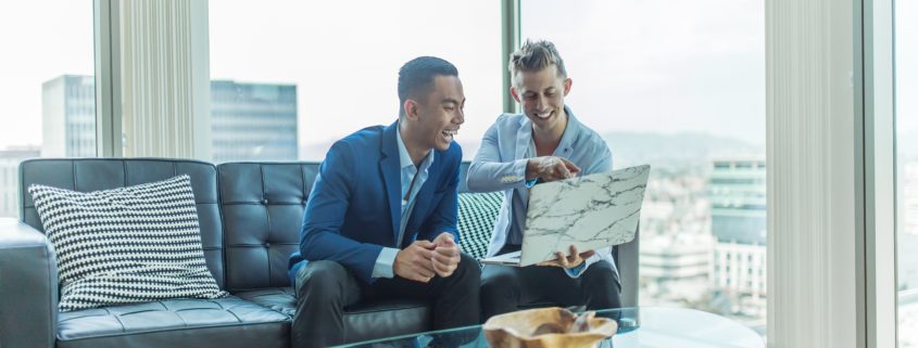 Two men on leather couch laughing at computer