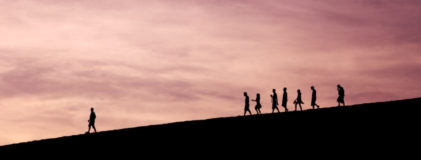 Silhouetted group walking over a hill with a leader in front