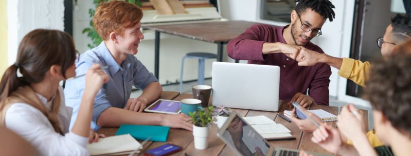 Group of young people sitting at a table and two men fist bumping