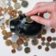 Hand putting coins into black ceramic piggy bank