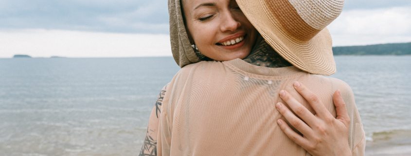 Tattooed woman hugging a friend on the beach